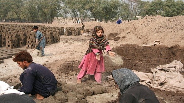 Zarghoona, 9, tosses sand on the ground to prepare it for making bricks with her father, brothers and sisters. The sand is used to prevent the mud bricks from sticking to the ground. [Khalid Zerai]