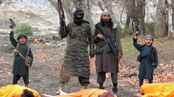 A screen shot from an ISIS propaganda video shows three dead prisoners and their ISIS killers, including children, brandishing their weapons.