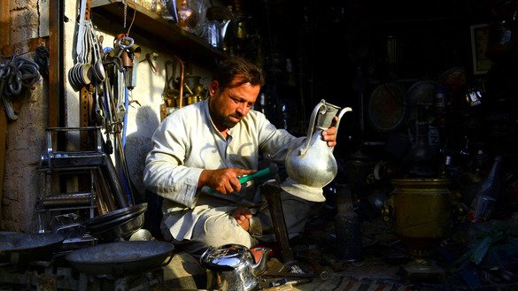 An Afghan man repairs a jug as he works at his shop in Herat Province on July 16. [Hoshang Hashimi/AFP]