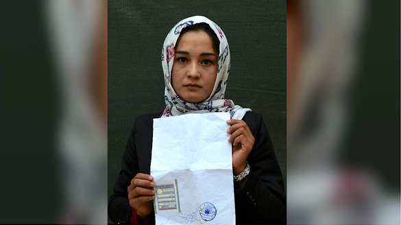 Kabul university student Zahra Faramarz, 21, poses for a picture October 11 as she holds her tazkira indicating she is registered to vote in the upcoming parliamentary election, in Kabul. [Wakil Kohsar/AFP]