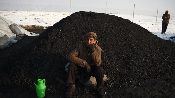A day labourer sits next to a pile of coal amid heavy smog on the outskirts of Kabul on January 8. [WAKIL KOHSAR/AFP]