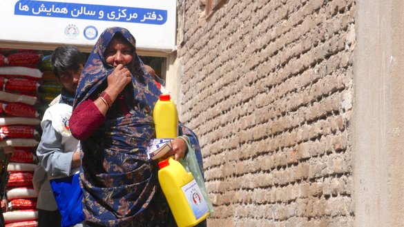 یک زن در شهر هرات به تاریخ اول ثور روغن را که از یک بنیاد خیریه دریافت کرده است انتقال می دهد. [عمر/سلام تایمز]