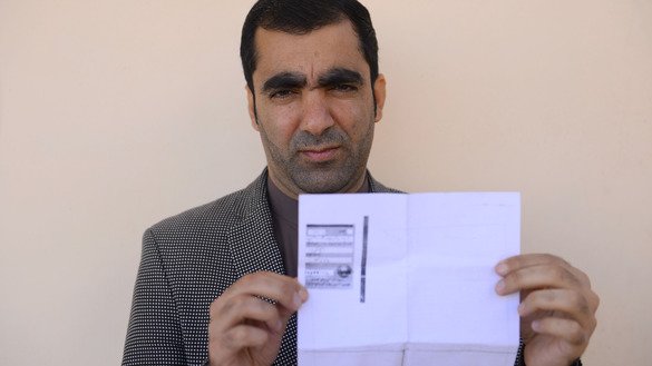 Public servant Ghulam Farooq Adil poses for a picture on October 15 as he holds his tazkira indicating he is registered to vote in the upcoming parliamentary election, in Herat Province. [Hoshang Hashimi/AFP]