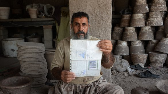 Shirin Agha, a 45-year-old potter, poses for a picture Ocotber 10 at his workshop on the outskirts of Jalalabad as he holds his tazkira indicating he is registered to vote in the upcoming parliamentary election. [Noorullah Shirzada/AFP]