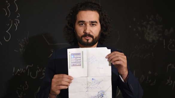 Afghan Co-founder and President of ArtLords Omaid Sharifi, 32, poses for a picture October 8 as he holds his tazkira indicating he is registered to vote in the upcoming parliamentary election, in Kabul. [Wakil Kohsar/AFP]