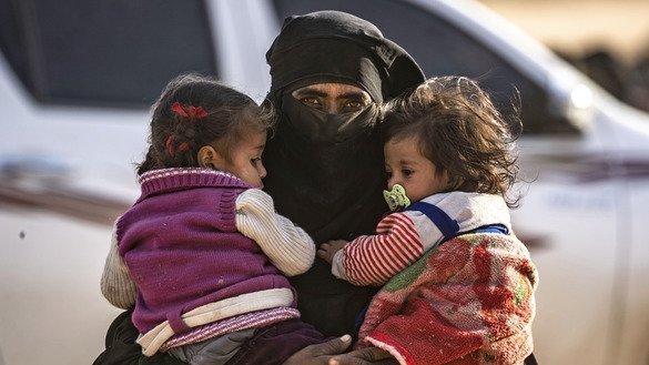 A fully veiled woman holds two little girls against her chest as hundreds of civilians, who streamed out of ISIS's last Syrian stronghold, walk towards a screening point for new arrivals run by US-backed Syrian Democratic Forces (SDF) outside Baghouz, Syria, March 5. [Delil Souleiman/AFP]