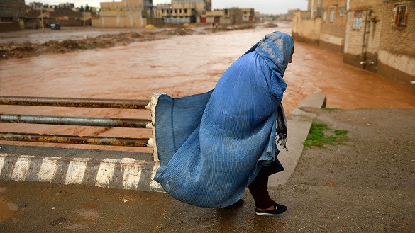 بتاریخ ۹ حمل، یک زن که برقع پوشیده در ولایت هرات پس از جاری شدن سیلاب از پل عبور می کند. [هوشنگ هاشمی/ خبرگزاری فرانسه]