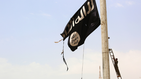 A member of the Syrian Democratic Forces removes an ISIS flag in Tabqa, Syria, in 2017. [Delil Souleiman/AFP]