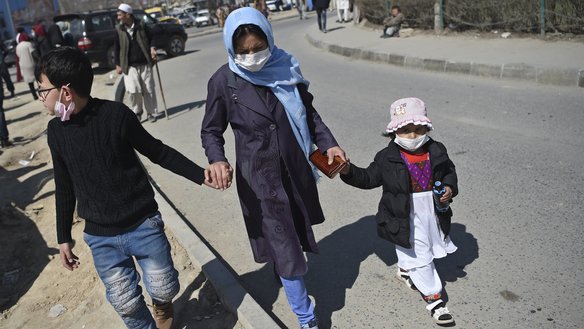 A woman with children wearing face masks as a protective measure against the spread of the coronavirus walk along a street in Kabul on March 18. [Wakil Kohsar/AFP]