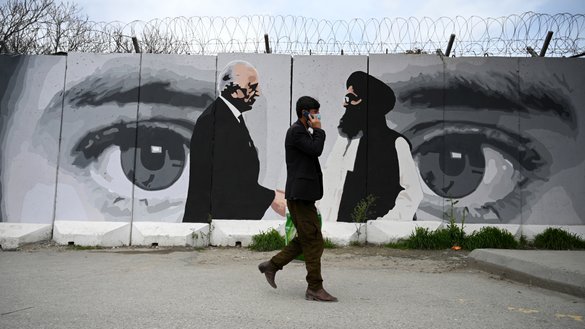 A man wearing a mask as a precautionary measure against the COVID-19 coronavirus walks past a wall painted with images of US Special Representative for Afghanistan Reconciliation Zalmay Khalilzad (left) and Taliban co-founder Mullah Abdul Ghani Baradar (right), in Kabul April 5. [Wakil Kohsar/AFP]