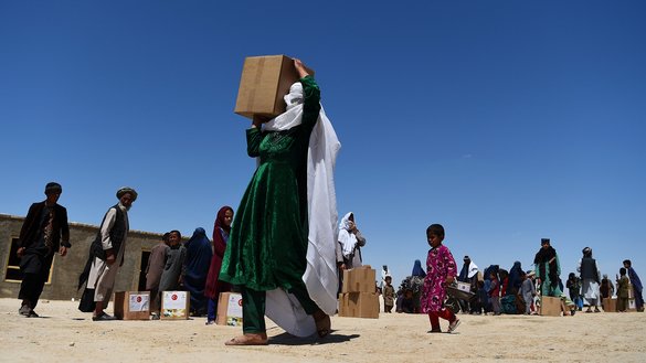 در تصویر دیده می شود که، یک زن بیجاشده داخلی به تاریخ ۱۴ ثور کمک رایگان را که در ماه مبارک رمضان در کمپ پناهندگان در حومه مزارشریف توزیع شده بود، روی شانه های خود حمل می کند. [فرشاد عصیان/ای اف پی]