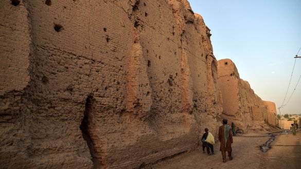 Internally displaced Afghan men and boys walk along the wall of a palace where they live along with other families at the historic site of Qala-e-Kohna in Lashkargah, the capital of Helmand province, on March 27. [Wakil Kohsar/AFP]