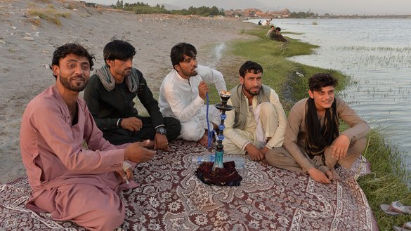 Men smoke a hookah water pipe along a river on the outskirts of Jalalabad on June 9. [Noorullah Shirzada/AFP]