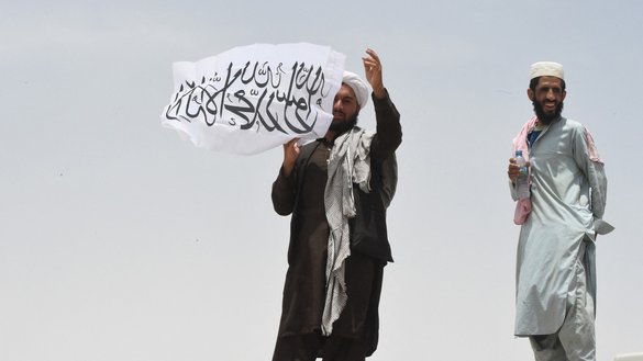 یک مرد که در طرف افغانستان مرز میان افغانستان و پاکستان ایستاده است، به تاریخ ۲۶ سرطان بیرق طالبان را در دست گرفته است. [بنارس خان/ای اف پی]