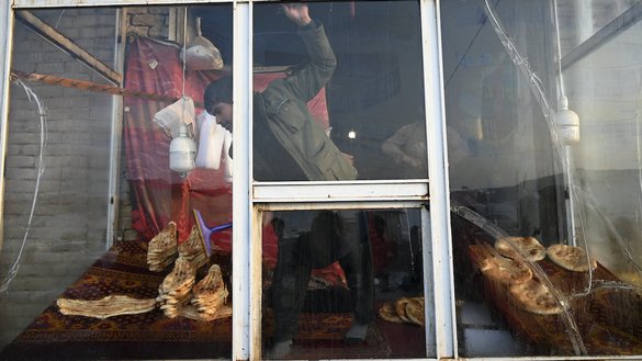 A baker cleans the window of a bakery as people wait to receive free bread distributed as part of the Save Afghans From Hunger campaign in Kabul on January 18. [Wakil Kohsar/AFP]