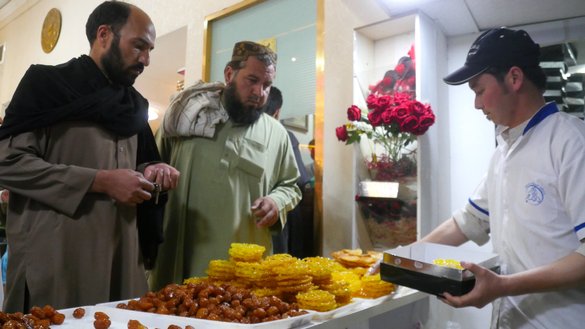 دو مرد در شهر هرات به تاریخ ۲ ثور از یک فروشگاه شیرینی می خرند. [عمر/سلام تایمز]