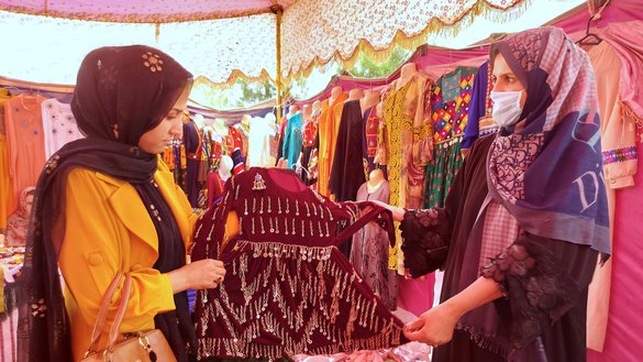 یک کارآفرین زن بتاریخ ۷ ثور در یک نمایشگاه تجارتی «از ما بخرید» در کابل، لباسی را به مشتری نشان می دهد. [سلیمان/سلام تایمز]