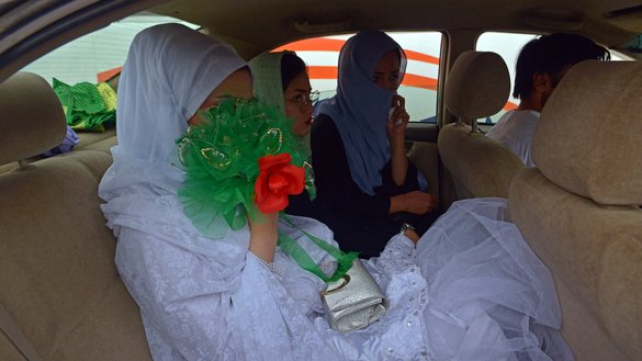 A bride (left) arrives in a car at the wedding hall for a mass marriage ceremony in Kabul on June 13. [Sahel Arman/AFP]