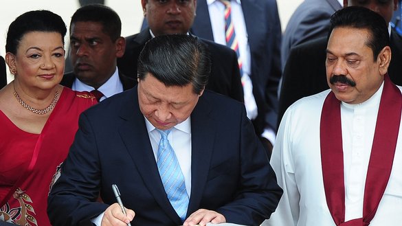 Chinese President Xi Jinping (centre) signs a visitor's book as then-Sri Lankan President Mahinda Rajapaksa (right) looks on during a welcome ceremony at the Bandaranaike International Airport in Katunayake on September 16, 2014. [Lakruwan Wanniarachchi/AFP]