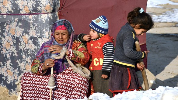 In this picture taken on January 17, an internally-displaced elderly woman along with two children sit outside their tent during a cold winter day at Nahr-e Shah-e-district, Balkh Province, near Mazar-i-Sharif. [Atif Aryan/AFP]