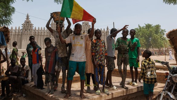 A youth shows the Malian nation flag during the re-plastering of the Great Mosque of Djenne on June 3, 2023. Al-Qaeda affiliate Jamaat Nusrat al-Islam wal-Muslimin has been expanding in Mali, preying on the country's youth as it lays waste to Islamic teachings. [Ousmane Makaveli/AFP]