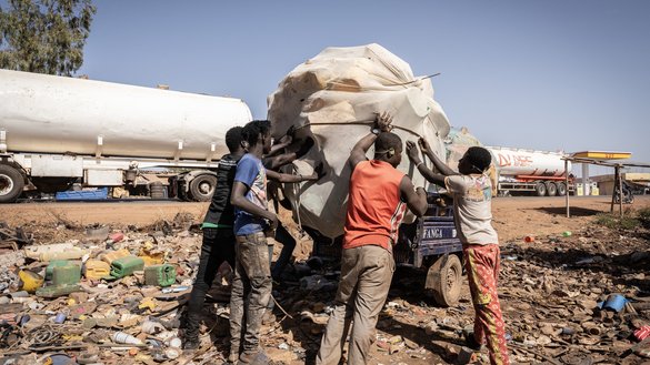Young people collect plastic for recycling as a fuel tanker convoy passes amid fuel shortages in Bamako on December 9, 2025. JNIM attacked fuel tanker convoys traveling through Mali in early December, mainly targeting routes from Senegal and Ivory Coast, causing economic hardship for local communities. [AFP]